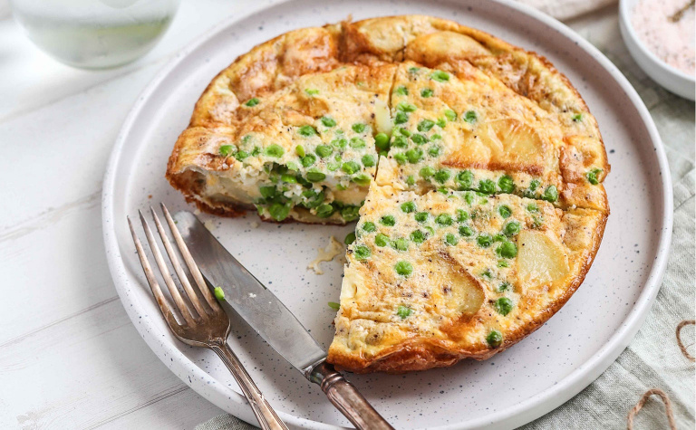 Image of a pea and potato frittata on a plate with a knife and fork.