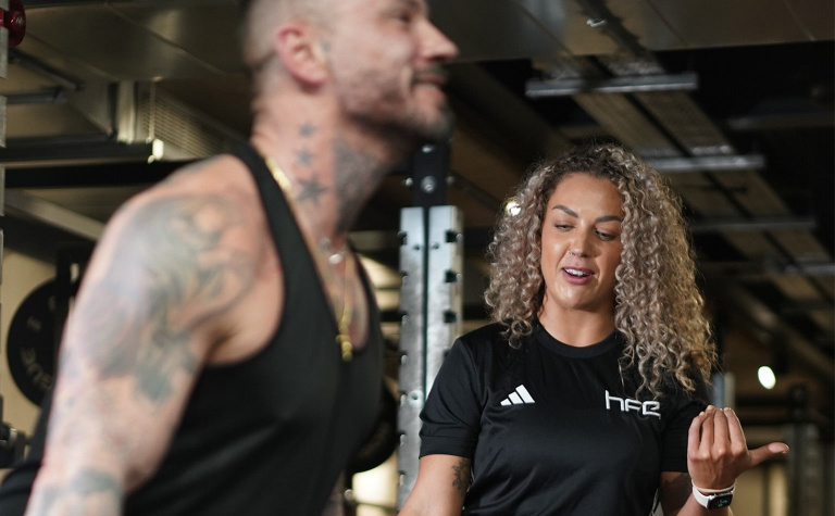 Female personal trainer helping client to lift a weight.