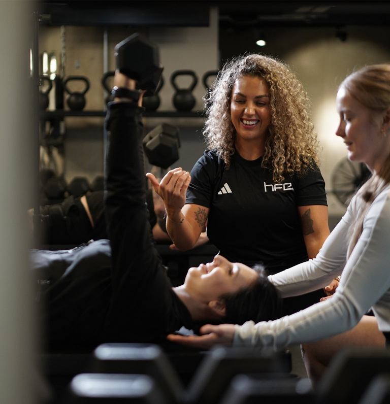 PT assisting 2 clients with a dumbbell chest press.